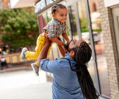 On a Baltimore street, a father lifts his young son up in the air. Both are smiling.